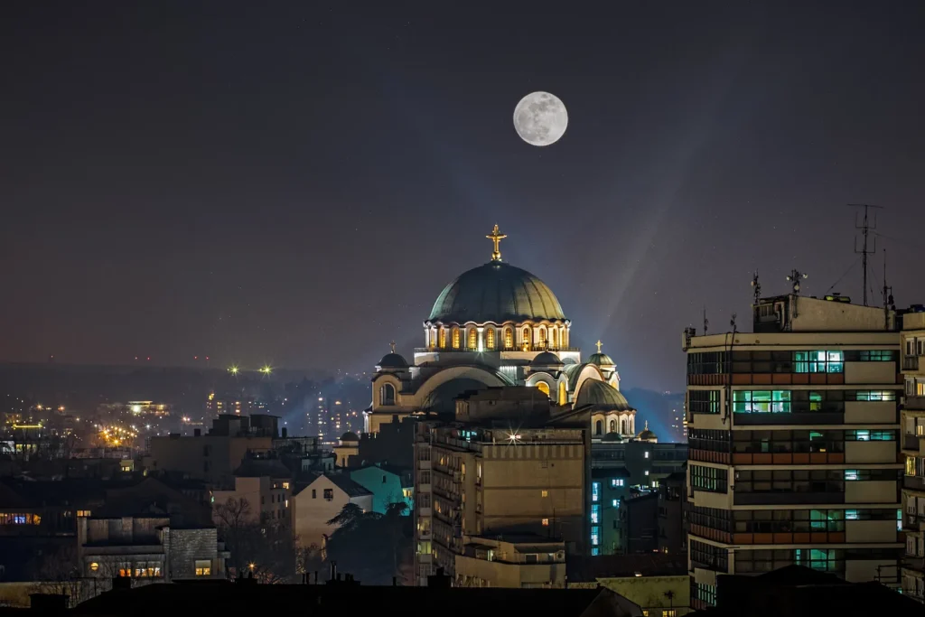 The Temple of Saint Sava lit at night under a full moon